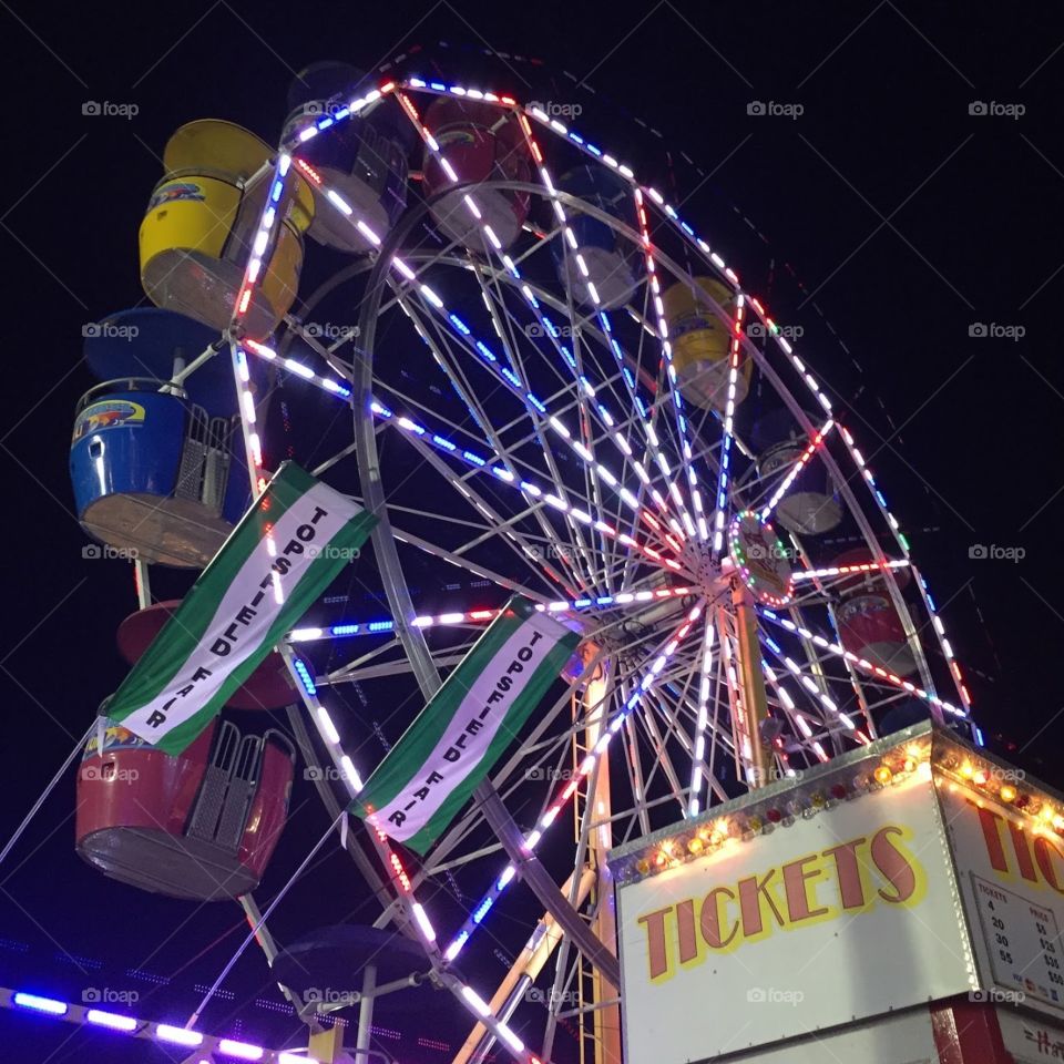 Ferris wheel lit up at night in front of ticket booth. 
