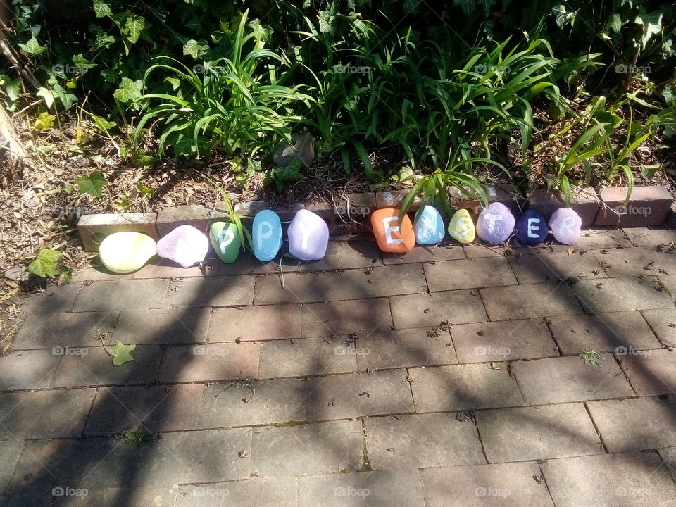 Stones in the neighbour's garden painted with Happy Easter for the Easter Weekend.