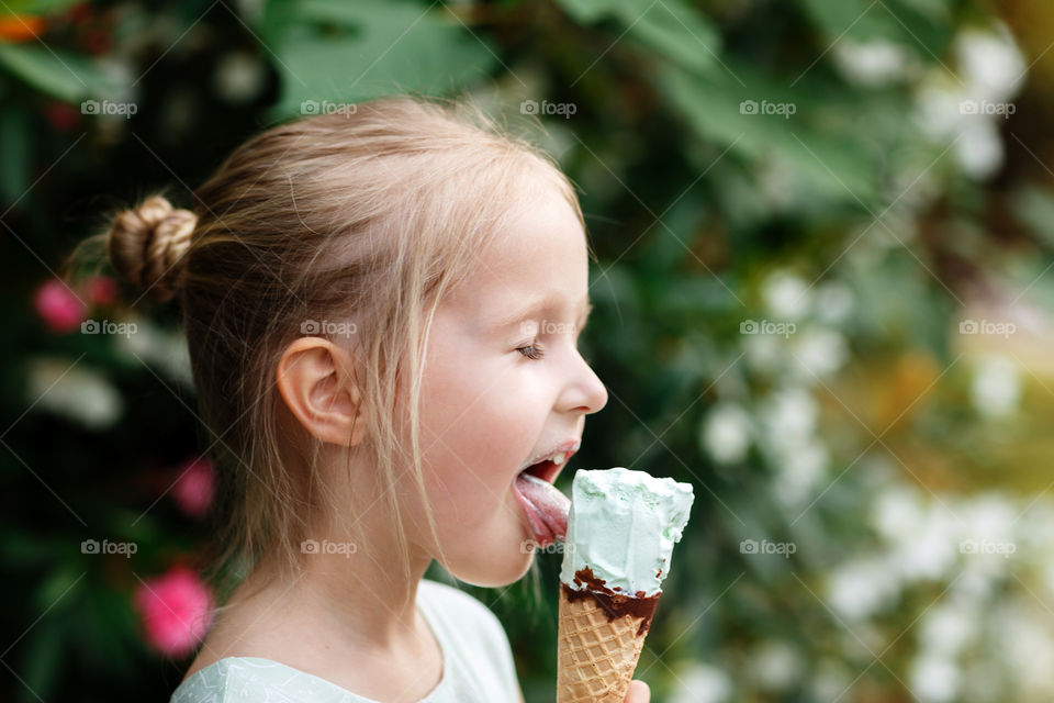 Little girl with blonde hair eating ice cream outdoor 