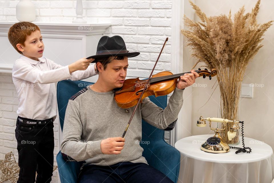 a young man plays the violin in a bright room, his son listens to music