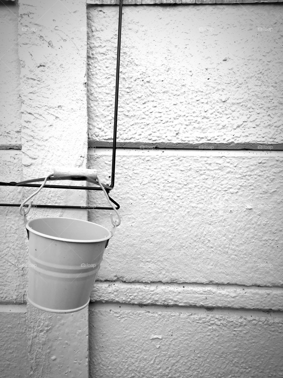 Empty planter bucket suspended on a bland grey wall. All it needs is a bit of green to brighten up the scene.