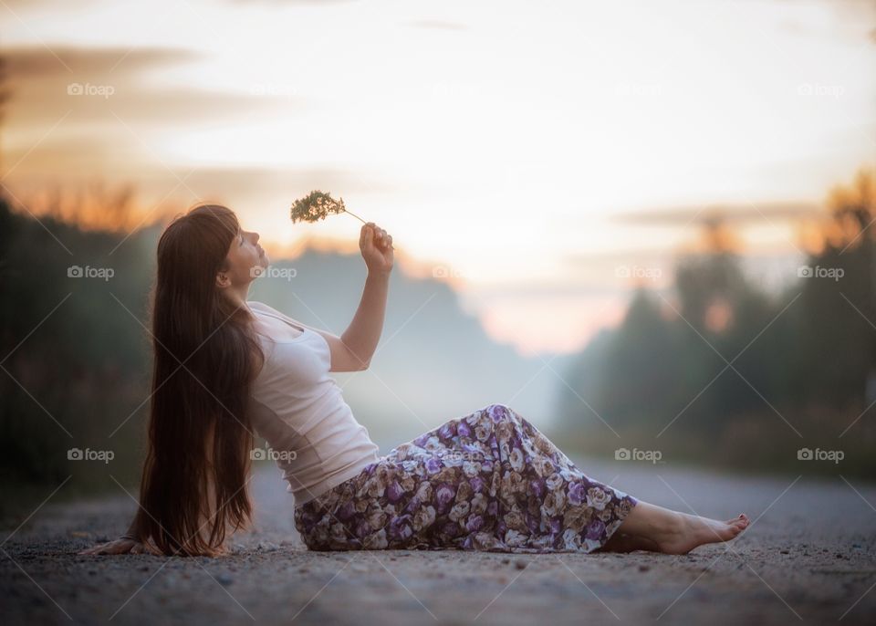 Beautiful young woman on the road at sunset in boho style