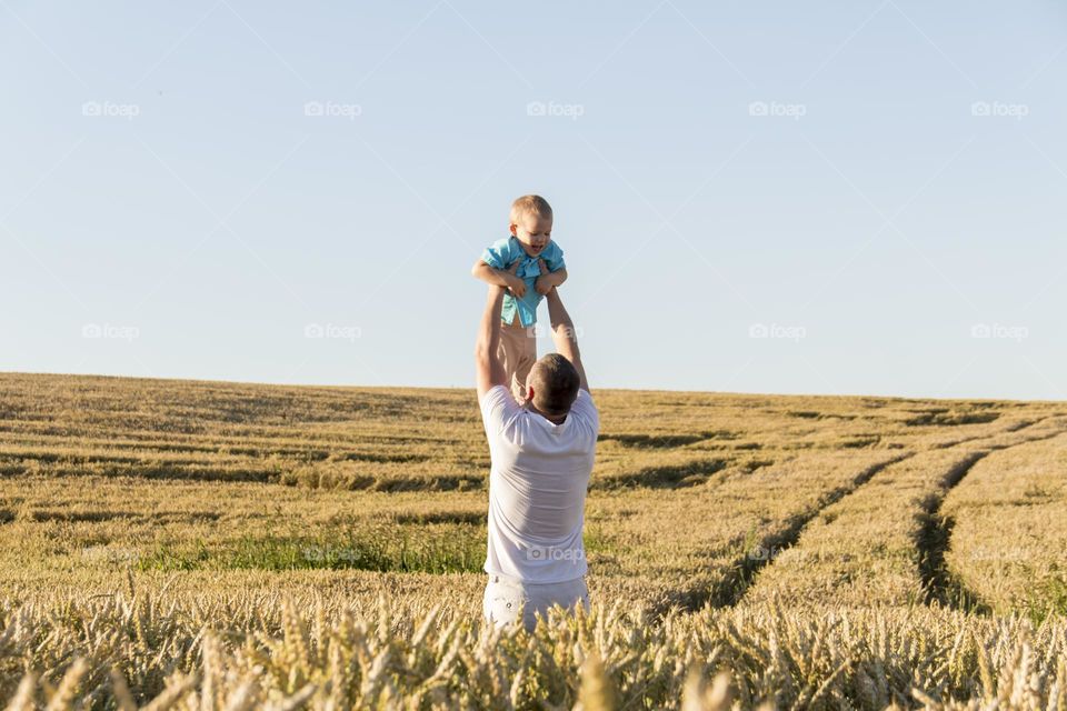Dad and son are walking in a field with ripe wheat during the harvest.