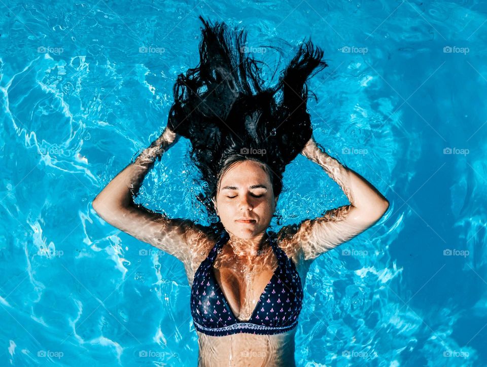 Top view of young woman with long dark hair floating in swimming pool