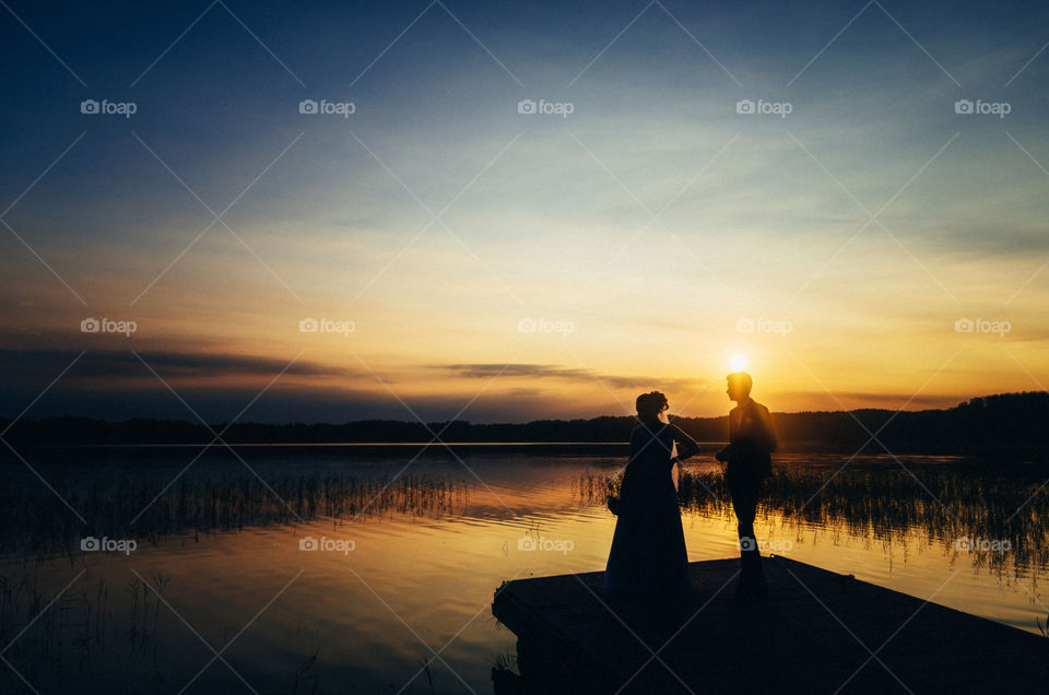 The wedding concept on the shore of a lake at sunset. The sun over the head of the groom.