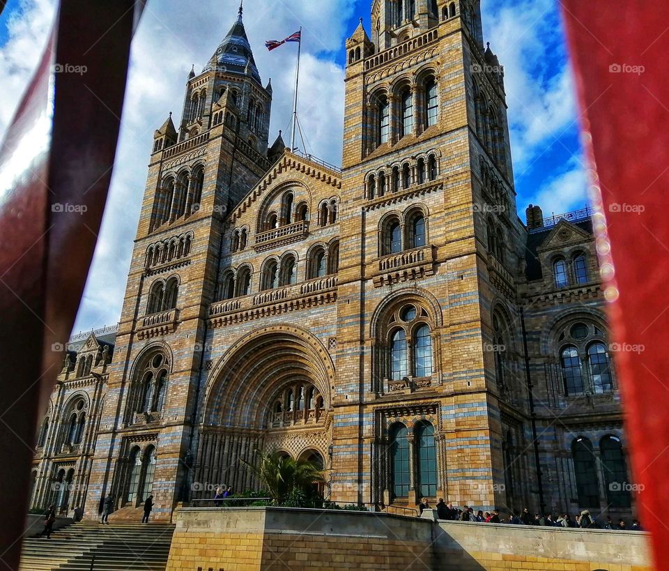 A photo of London's famous Museum of Natural history with its stunning architecture captured from between the red metal fence at the entrance