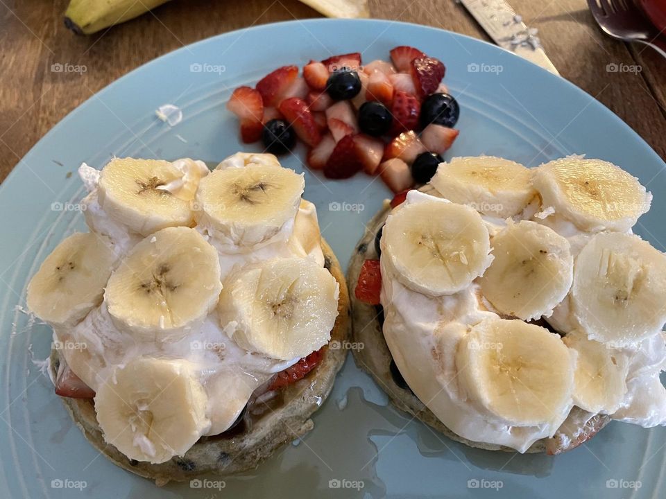 There are a few circles in this picture, first the circle teal plate, next the blueberry waffles, then the whip cream topped with circle bananas, and then lastly the blueberries in the mixed fruit salad