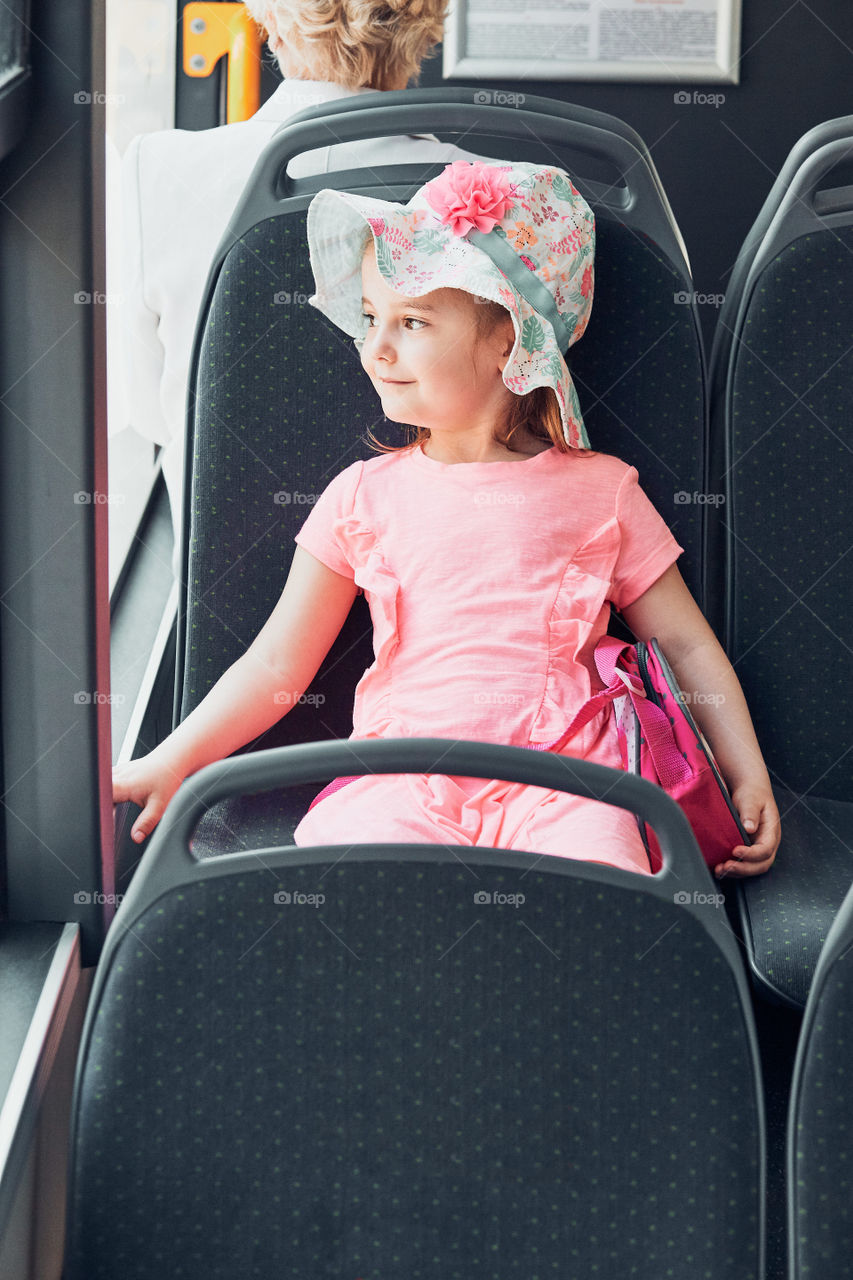 Little adorable girl travelling by electric bus. Child sitting in a city bus looking through the window. Ecological public transport. Real people, authentic situations