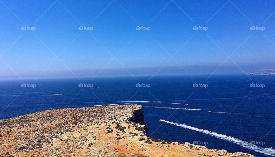 Standing on a cliff overseeing boats , the ocean and horizon