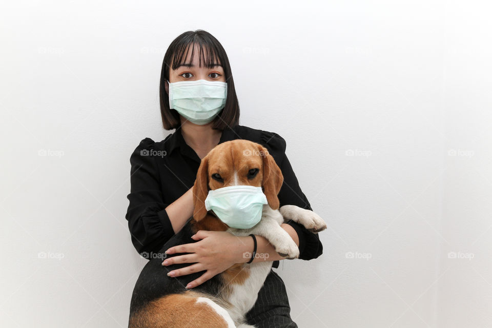 Lovely young woman hugging her cute beagle dog both wearing Covid protective mask  to stay safe