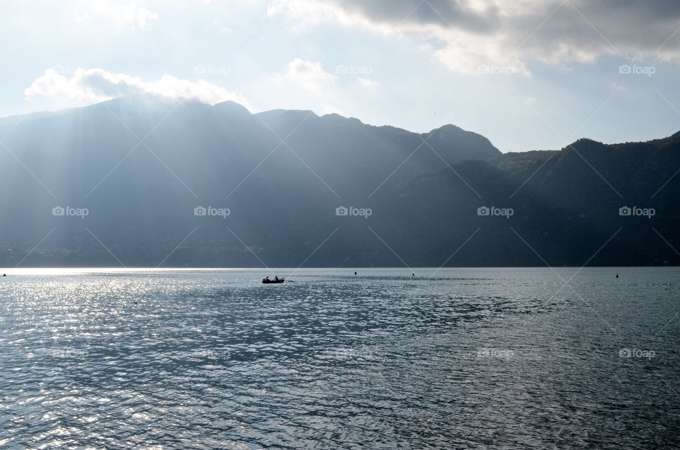 Lake and sunlight through mountains with a boat. Lake and sunlight through mountains with a small boat in silhouette 
