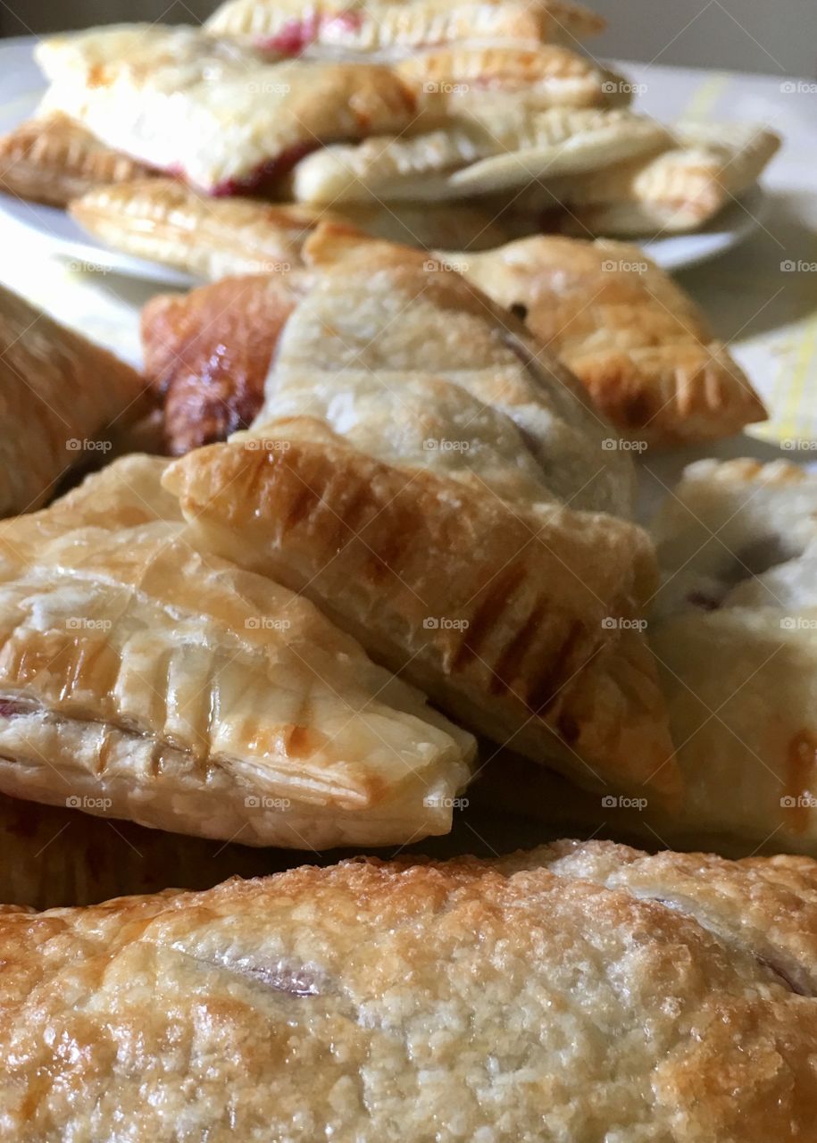 Fresh baked fruit strudels turnovers using puff pastry closeup many grouped on plates 