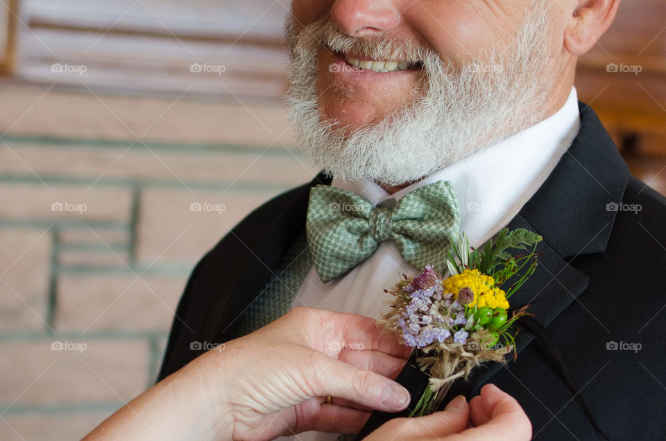 Dad gets his wildflower boutonnière pinned on by his wife as he prepares to walk his daughter down the aisle 