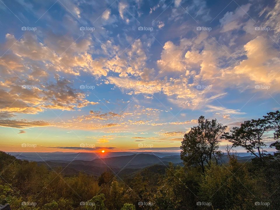 Clouds mission - the sun sets over the Blue Ridge Mountains, a tiny speck in the big sky filled with dreamy clouds and colors 