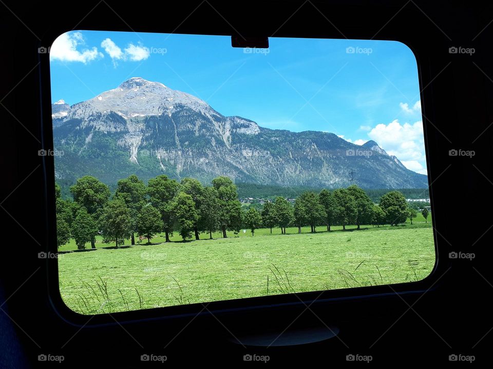 Bright and sunny landcape of mountain and lush trees seen from a train window  in Austria. This small european country offers fantastic mountain views, interesting traditions and cuisine, with endless outdoors activities. Strongly recommend!