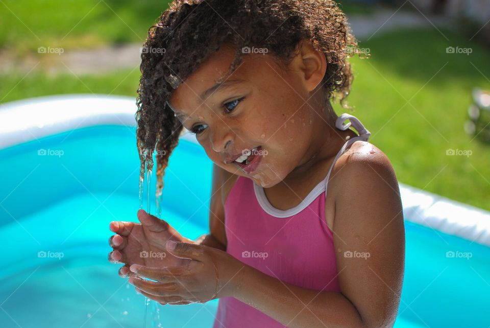 Cute little girl enjoying some playtime in a swimming pool during a hot summer day, looking for refreshment