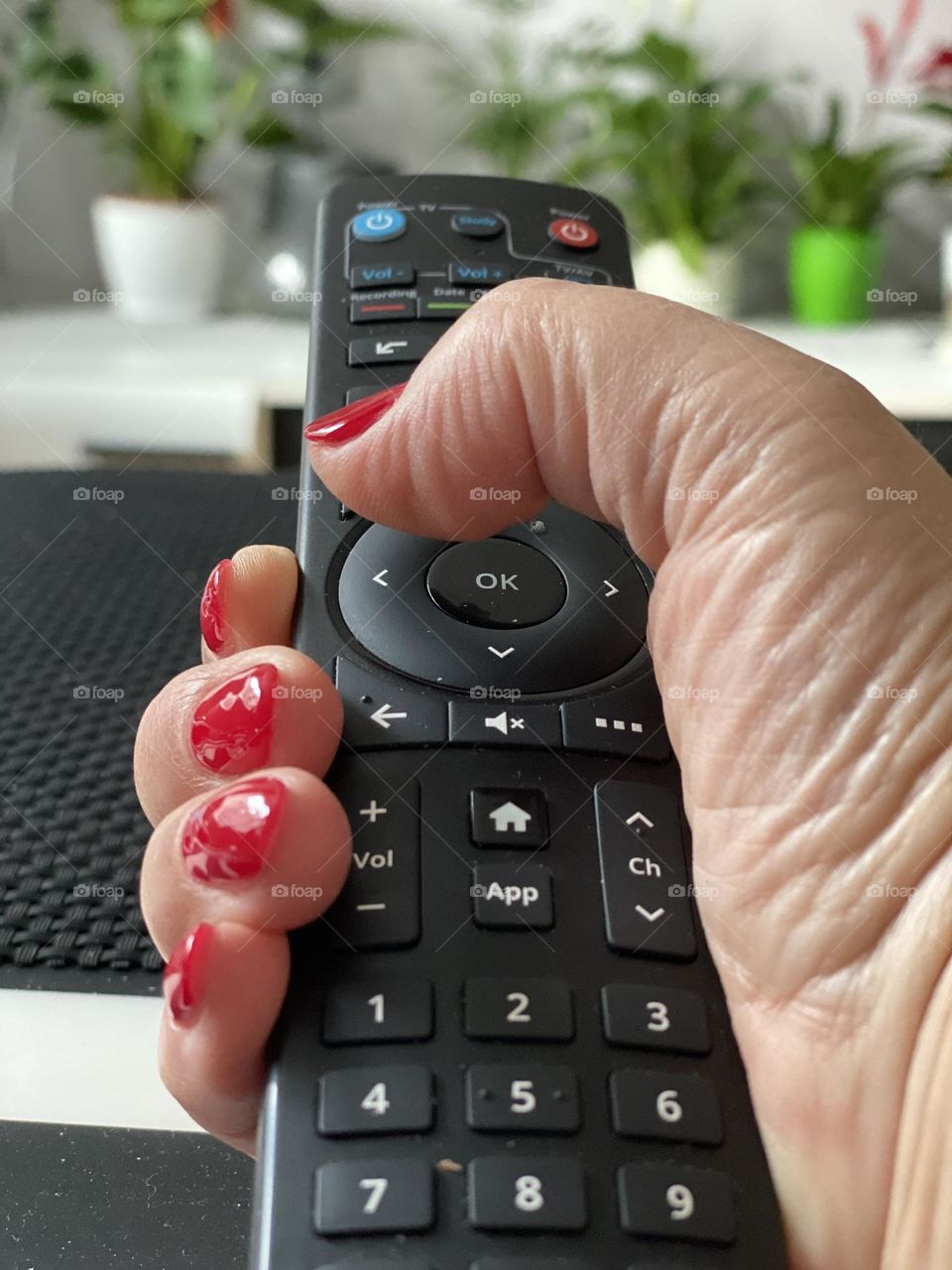 Hand with red manicure holding TV remote 