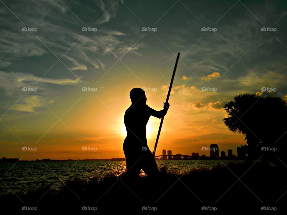 Give Me Light - A silhouette of a young man with a stick, walks along the bay with a spectacular lighted background 