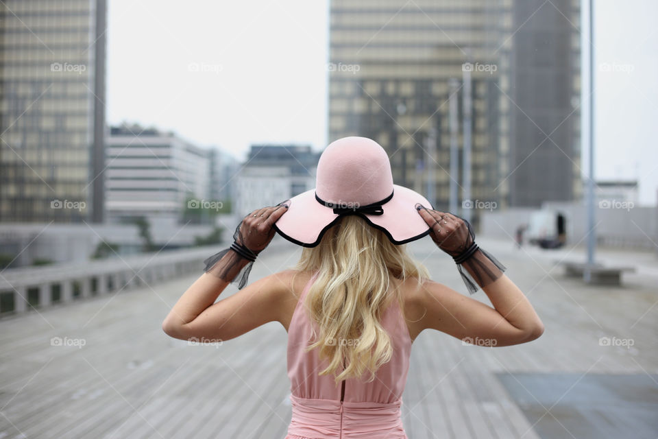 Faceless girl in pink dress and pink hat stands alone