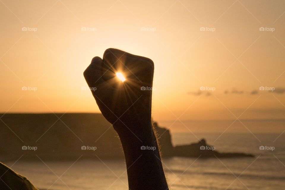 Silhouetted hand holding the sun during sunset 