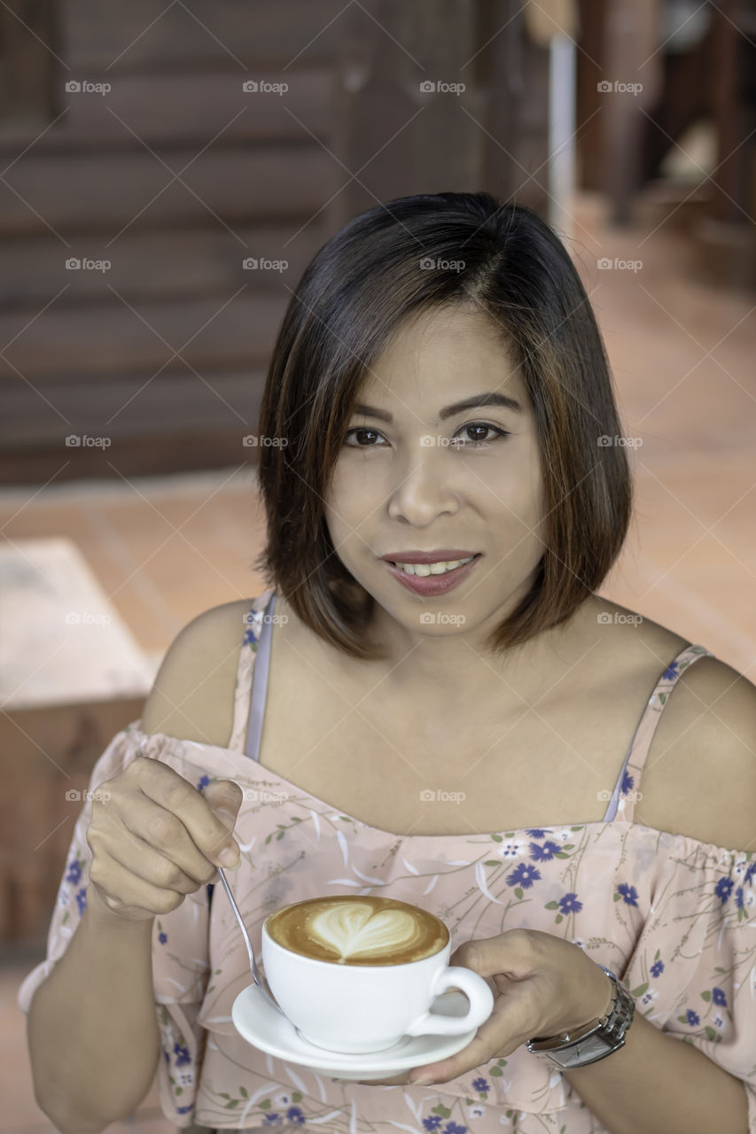 Hand Asian woman holding Hot coffee Espresso topped with a heart-shaped milk in white glass.