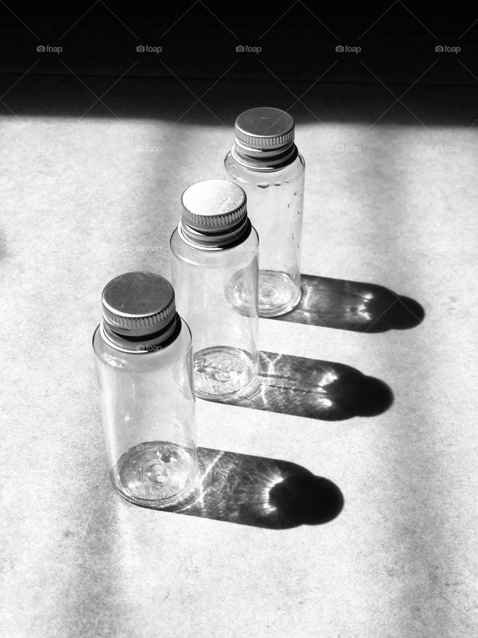 Black and white picture of three Empty bottles in a row and their shadow on the floor.