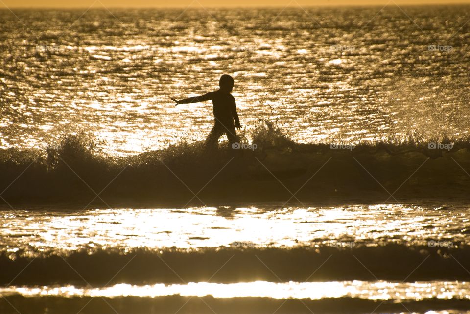Young boy surfing on small waves on the southern California shoreline during the summer near sunset