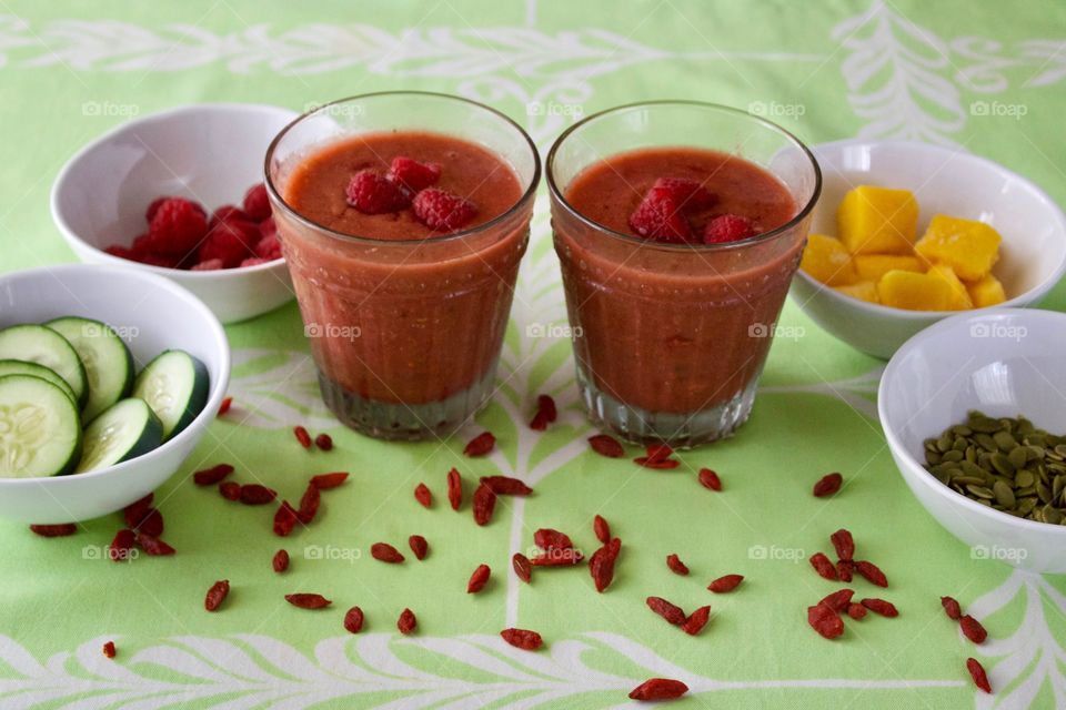 Healthy Smoothie Recipes - raspberry, cucumber and mango smoothies topped with fresh raspberries, pumpkin seeds or goji berries, on a light green tablecloth
