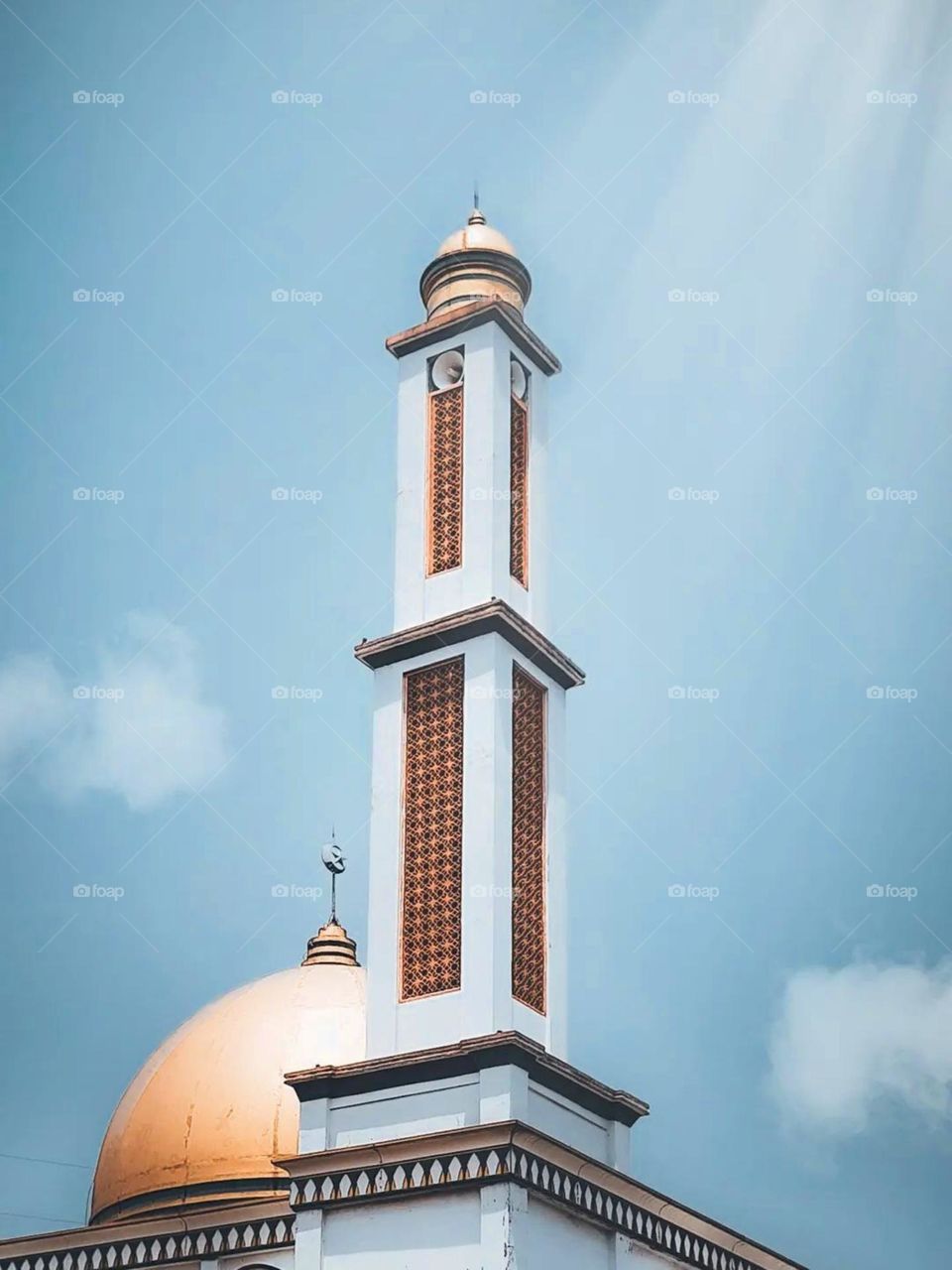 Close-up view of the top of the mosque with its golden dome and tall minaret in low angle view