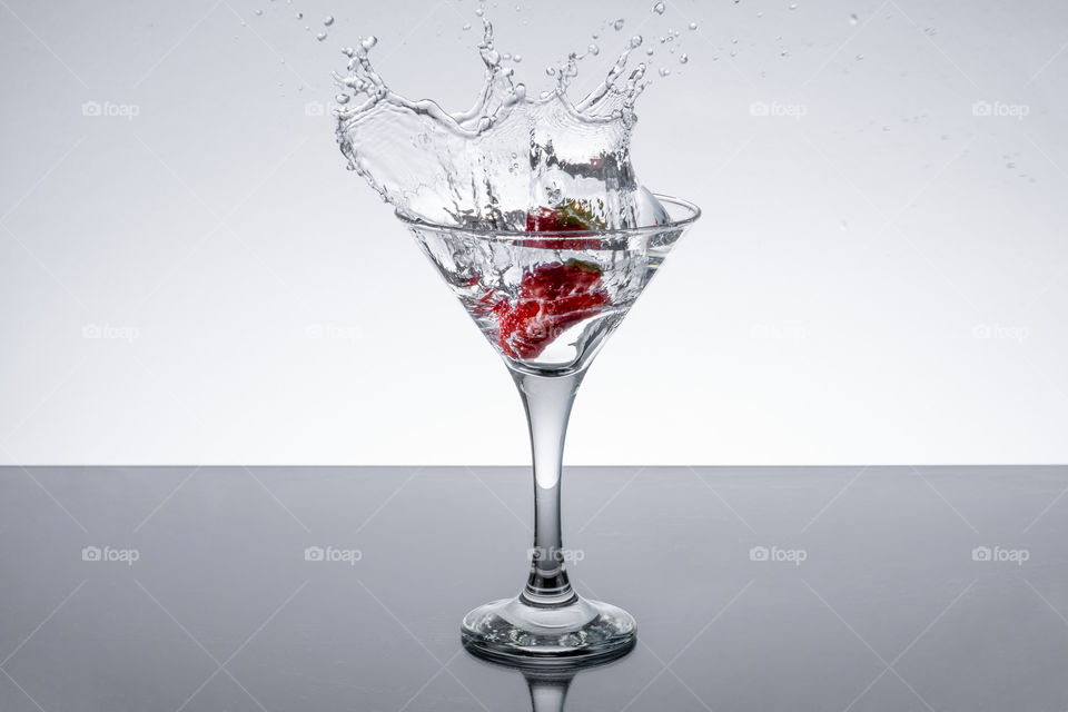 Fresh strawberry falling into glass of water
