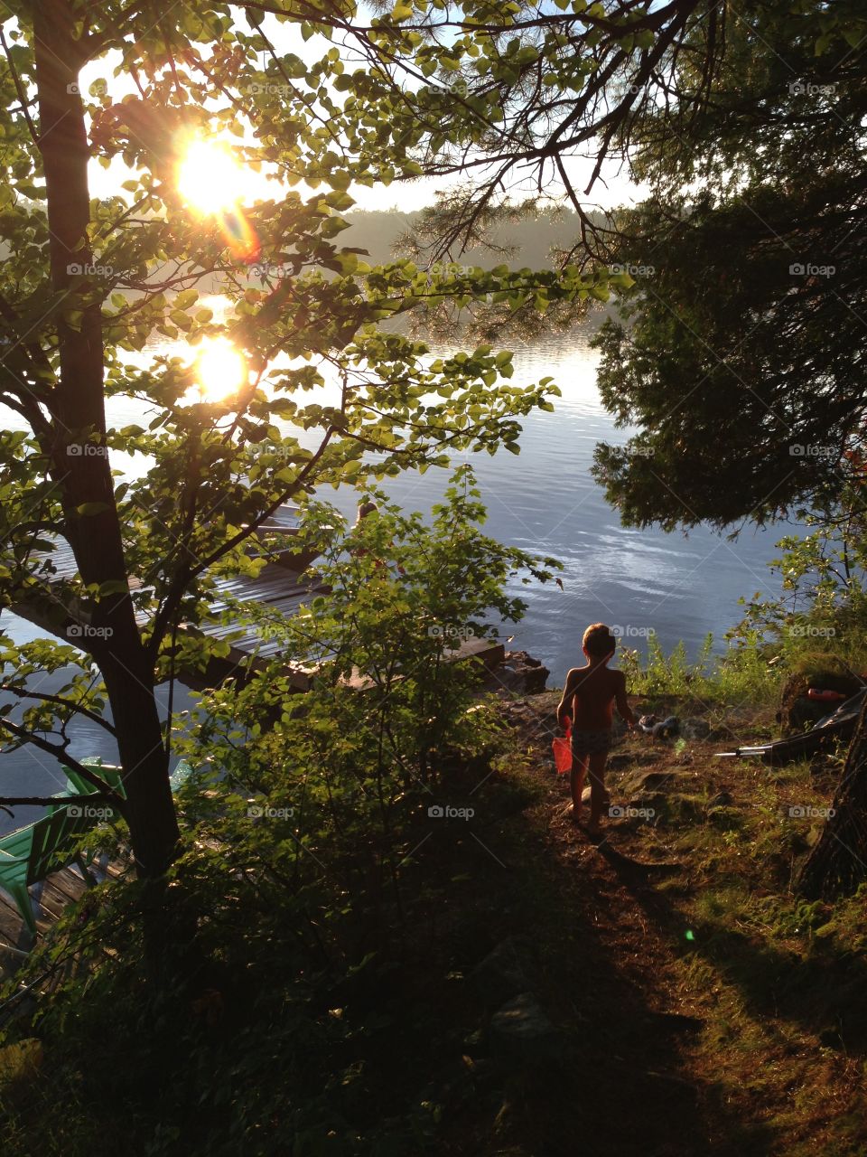 Lake house sunset. Little boy walking down to the dock at sunset