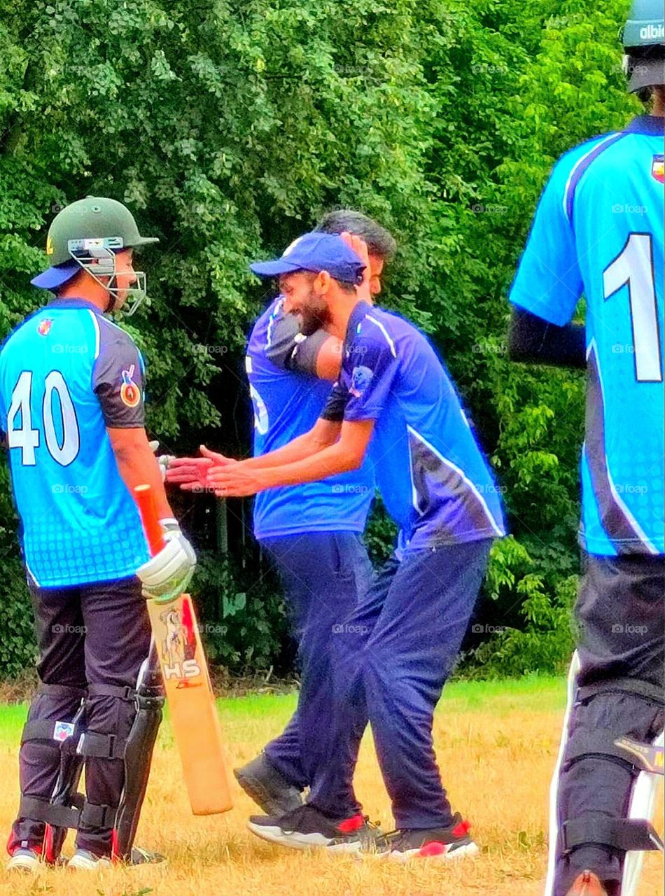Happiness.  On the field players in the game of cricket.  One man is dancing and laughing.  Pose and smile emotions of happiness