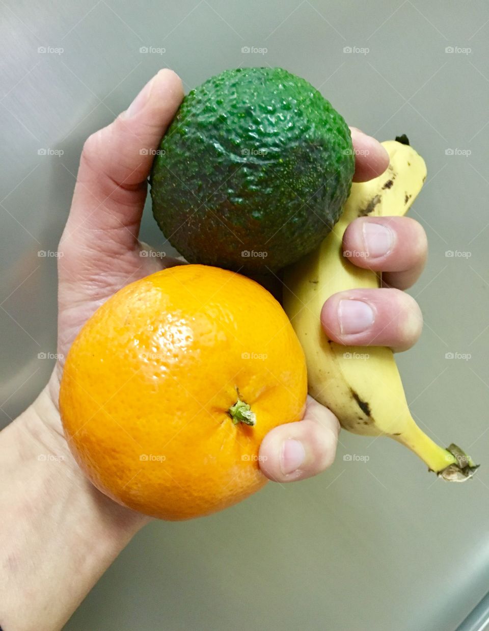 Hand holding avocado, tangerine and banana