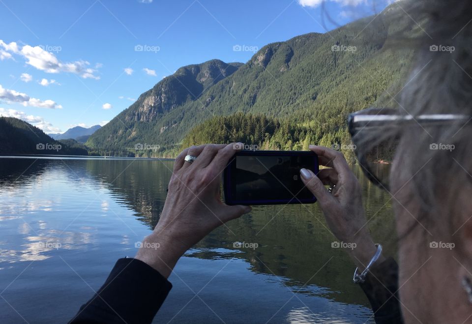 Middle aged Woman taking photo with smartphone of beautiful mountain lake scene