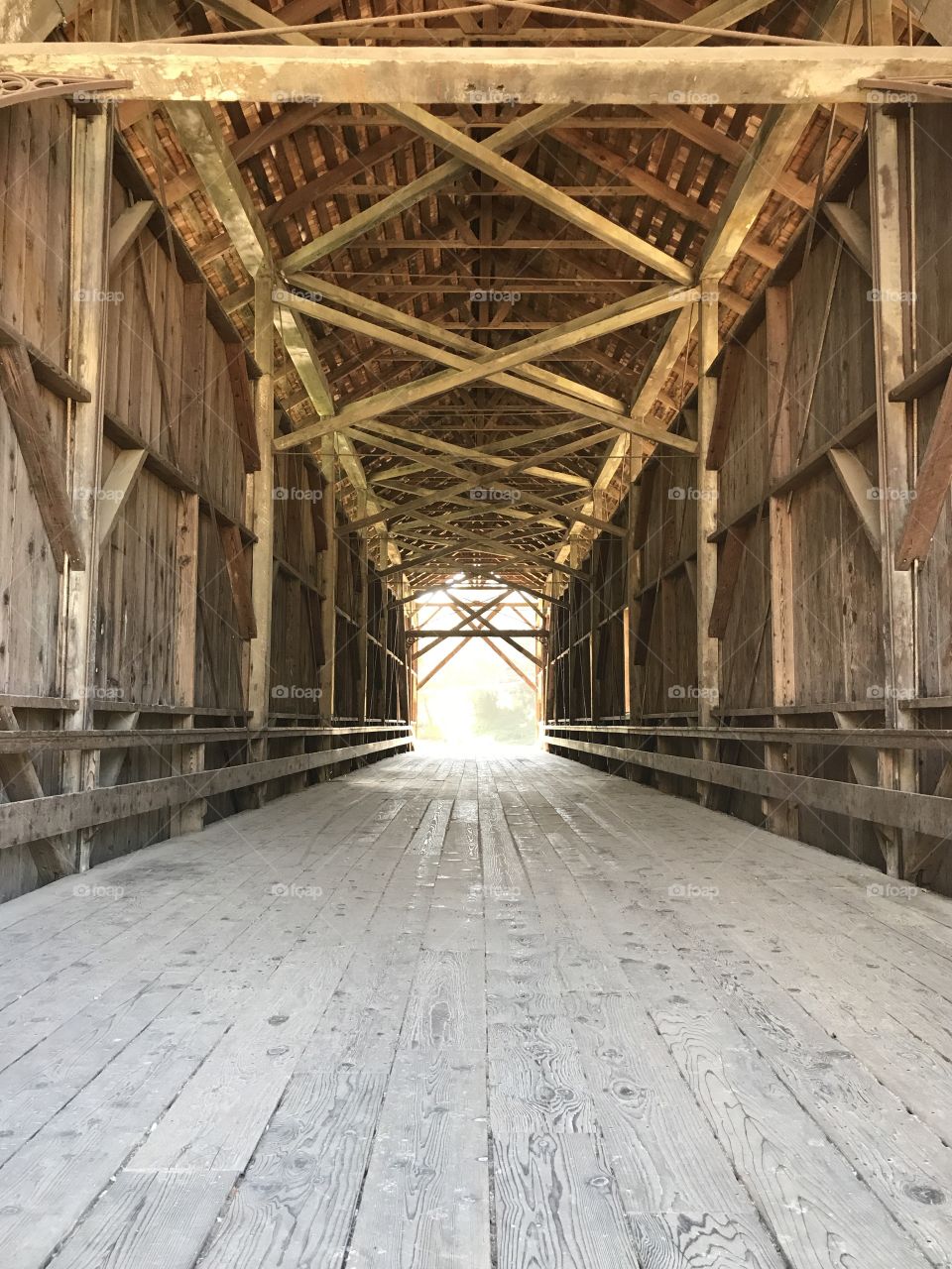The criss-crossing wooden beams of an old covered bridge, sunlight beaming at the end. 