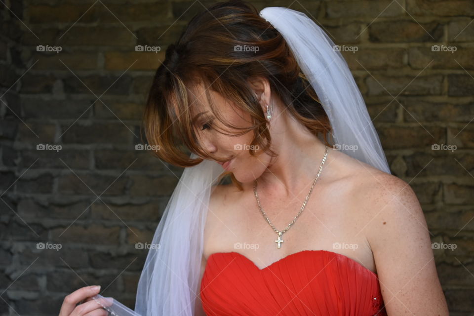 A bride to be admires her borrowed veil, dressed in a scarlet red gown. 