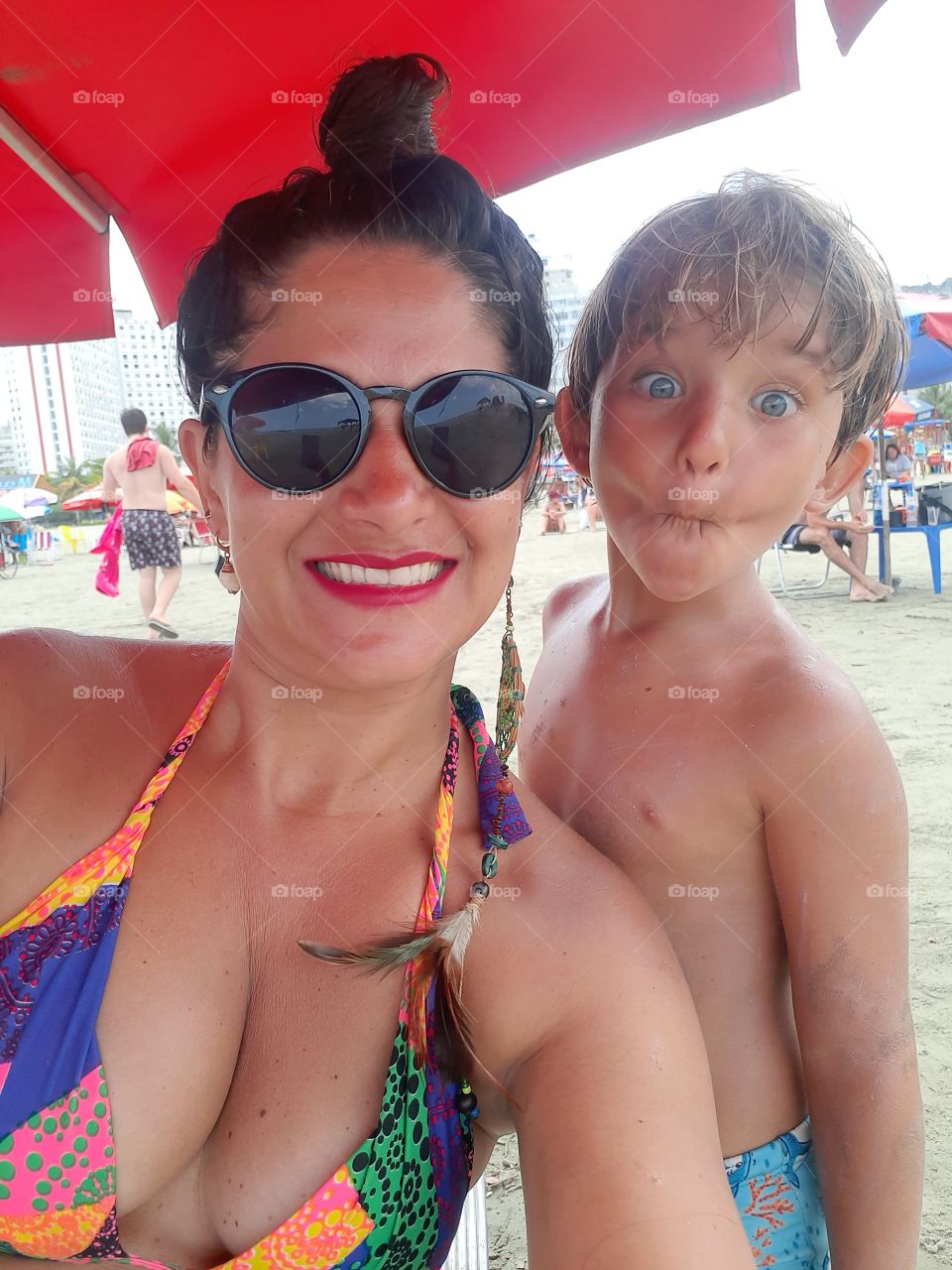 smiling woman with her son grimacing on the beach.
