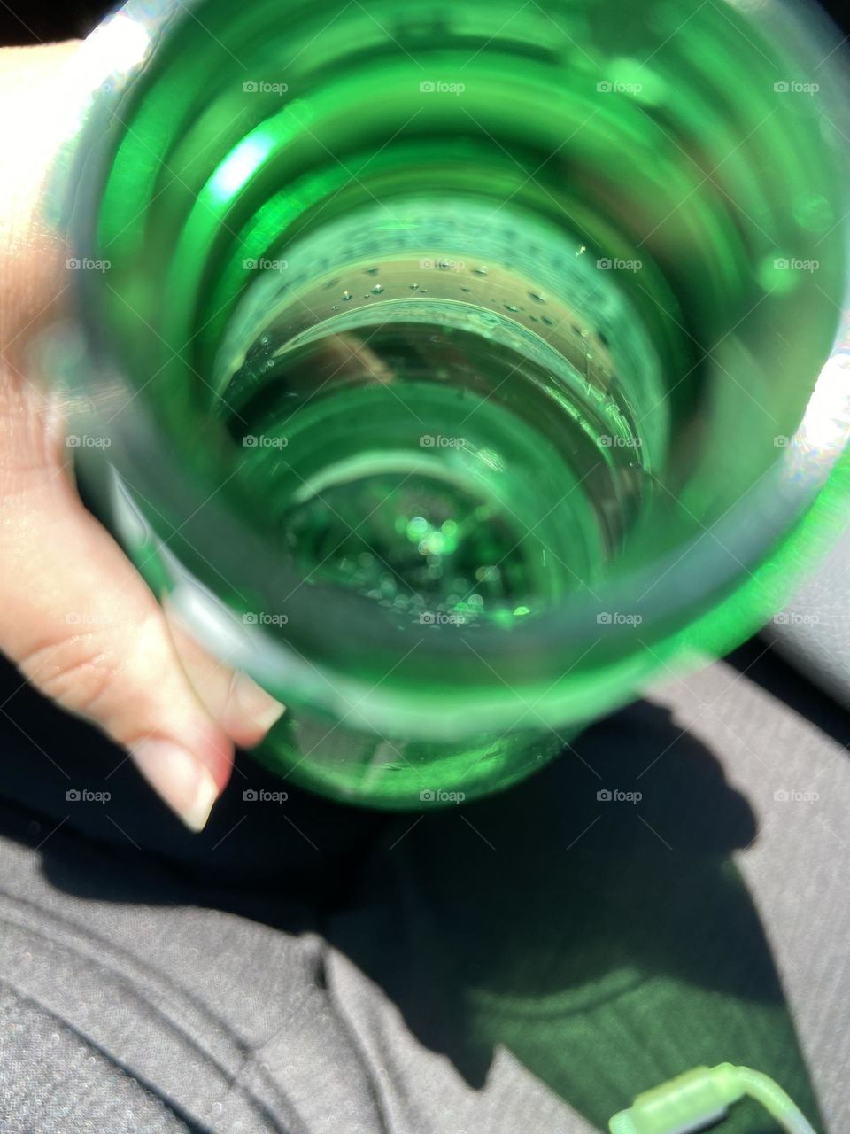 Holding a bottle of San Pellegrino sparkling water on a hot summer day. Bubbles can be seen in the water at the bottom and around the edges of the bright green bottle.  