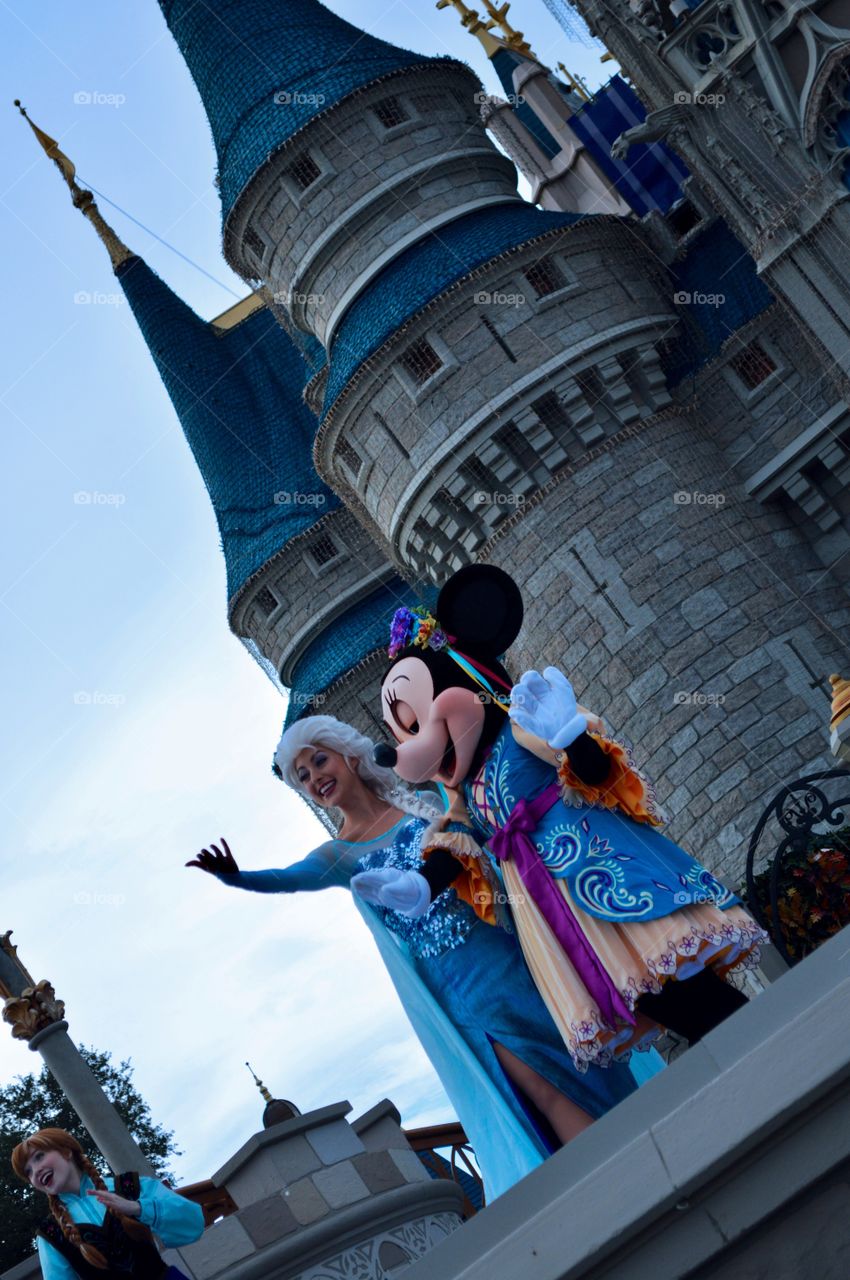 Fashionable woman standing with mickey mouse in front of castle