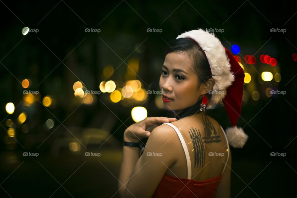 Pretty Asian Thai girl wearing sexy santaclaus outfit for Christmas party theme celebration at night on a fairy lights bokeh background