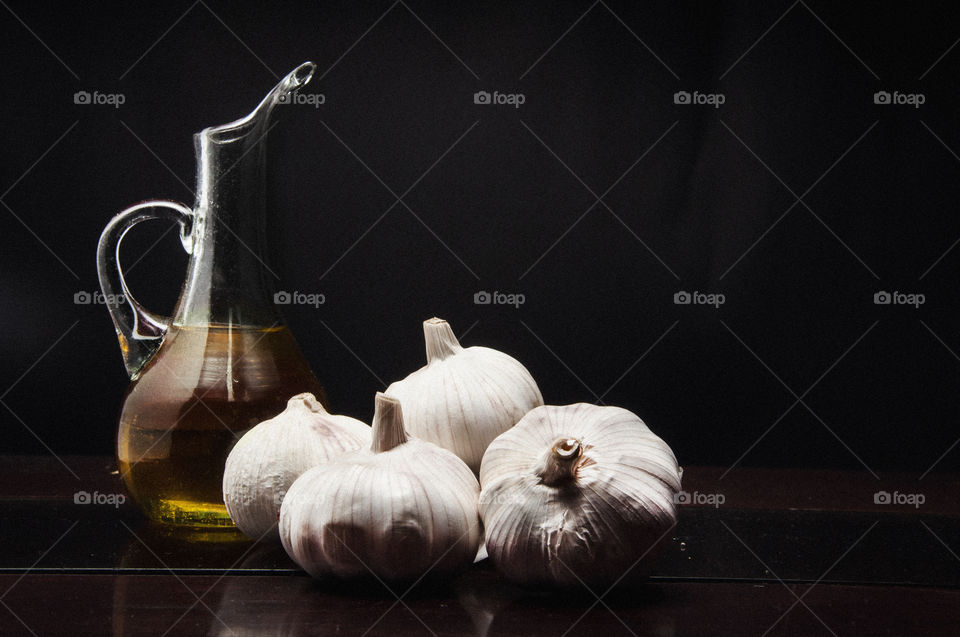 Olive oil jar besides fresh garlic cloves with a black background