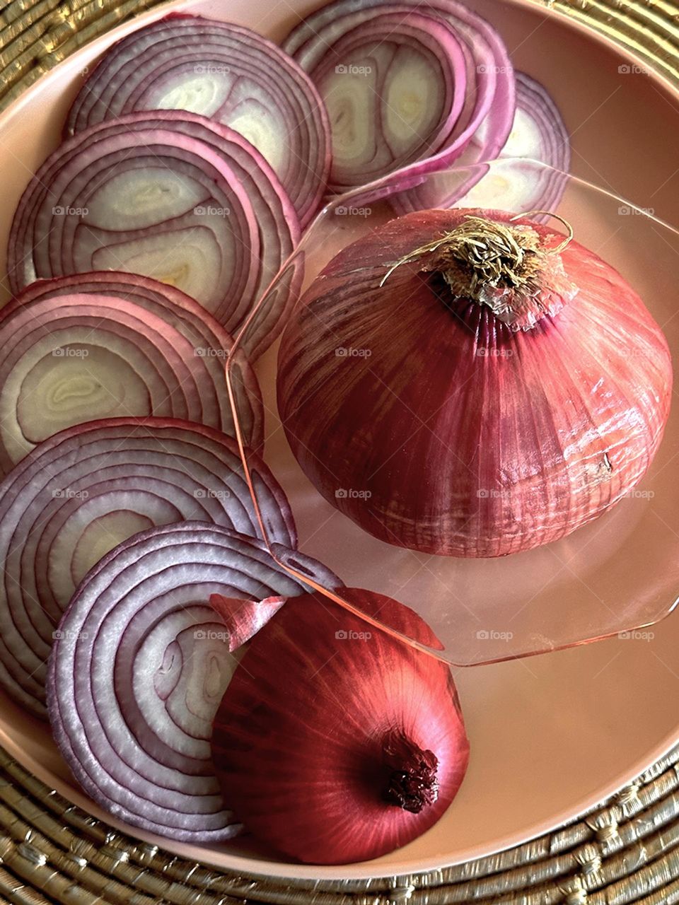 Sliced and whole red onions on a plate placed on a spiral woven placemat