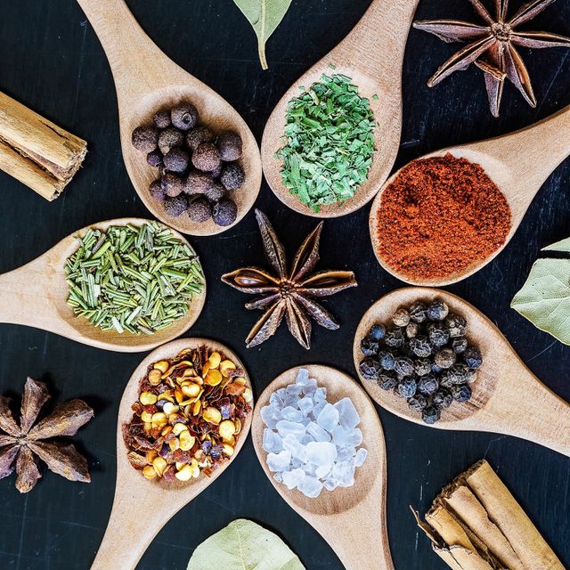 Various herbs and spices in wooden spoons on a black wooden background