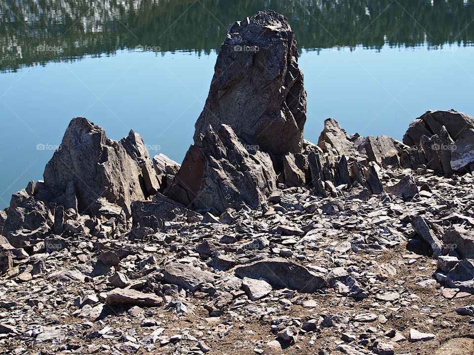 Jagged rocks and boulders along the shoreline of Ochoco Lake in Central Oregon on a sunny spring day.