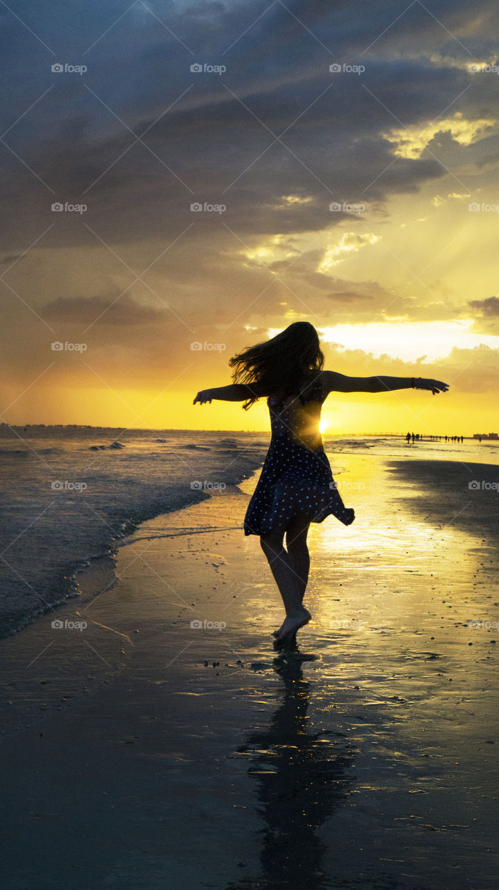 A young girl spins in a polka dot dress during sunset on a beach for fun