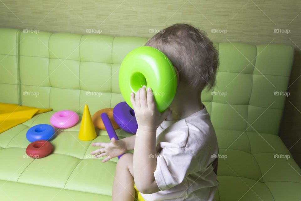 The child is having fun playing a bright pyramid educational toy, sitting on a green sofa.