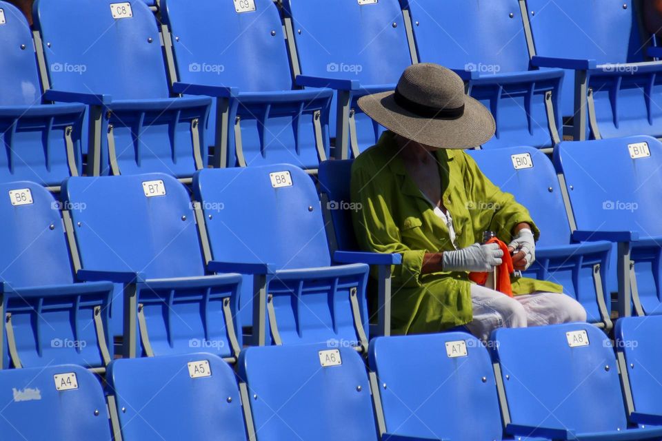 Lady is sitting on blue chairs for tennis spectators