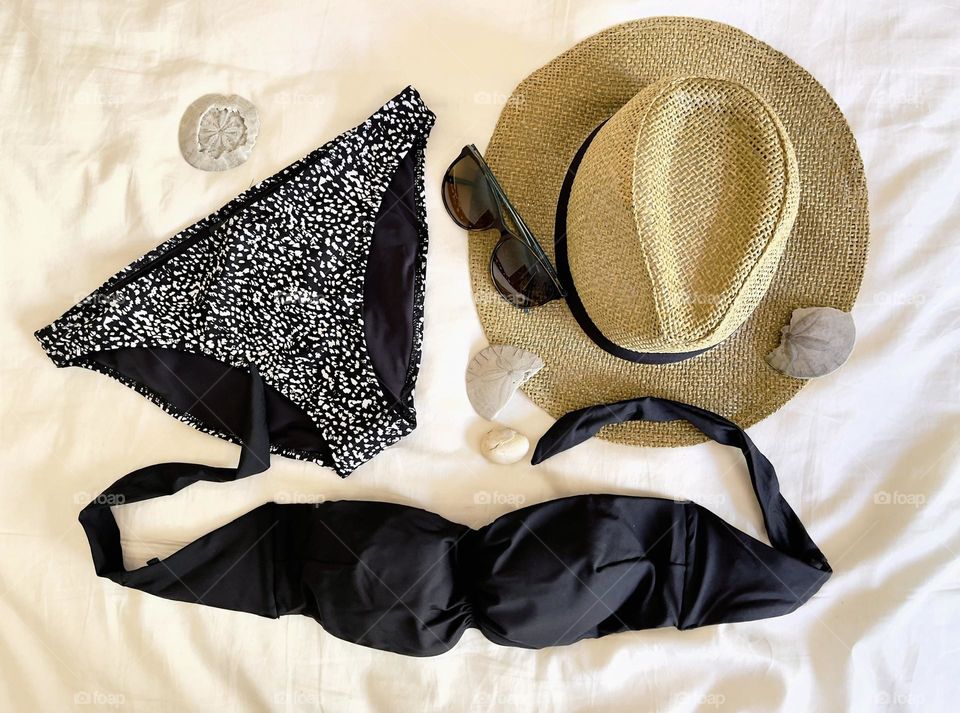 Black swimming suit, straw hat, sunglasses, shells, top view. Summer set