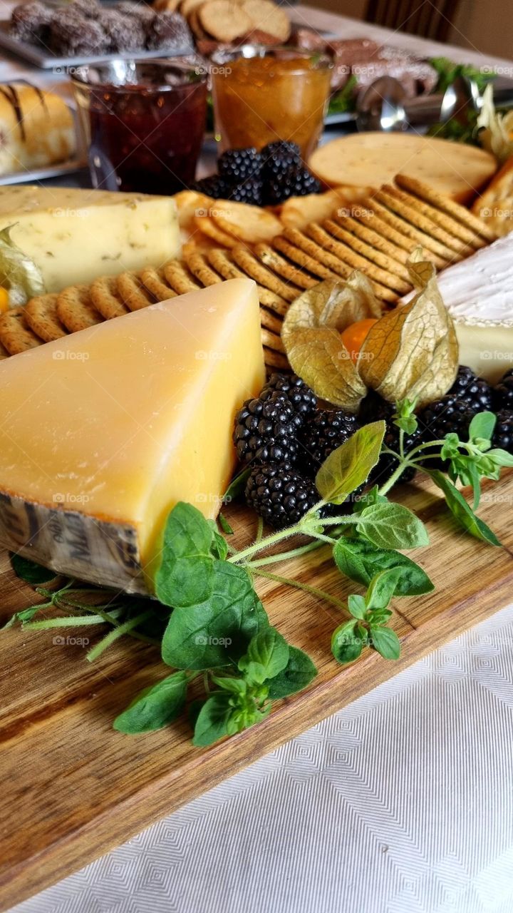 At the party, there is a cheese plate with several different delicious cheeses, different biscuits, jams and blackberries