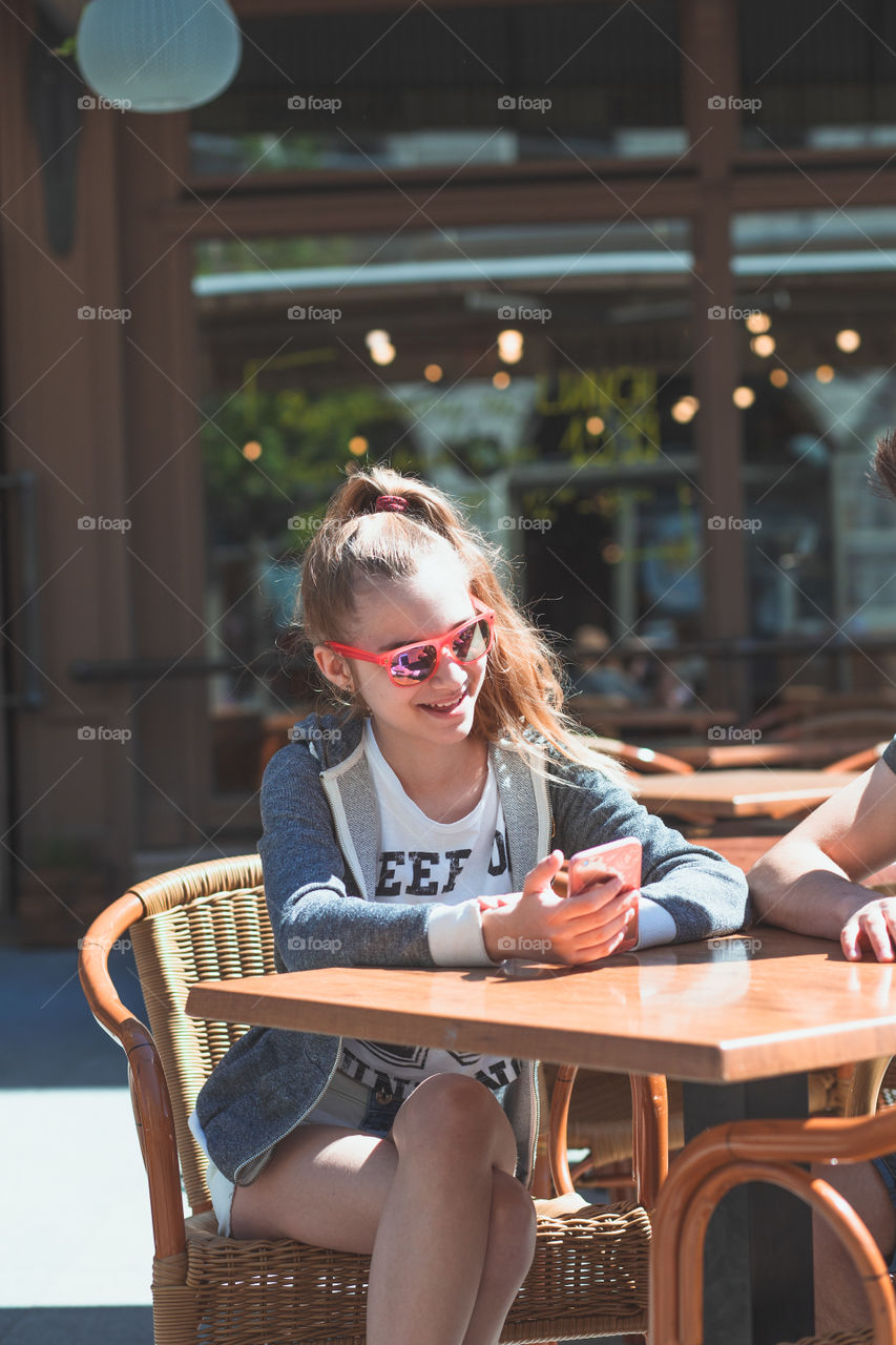 Young woman and man sitting in pavement cafe a the table talking and using mobile phones